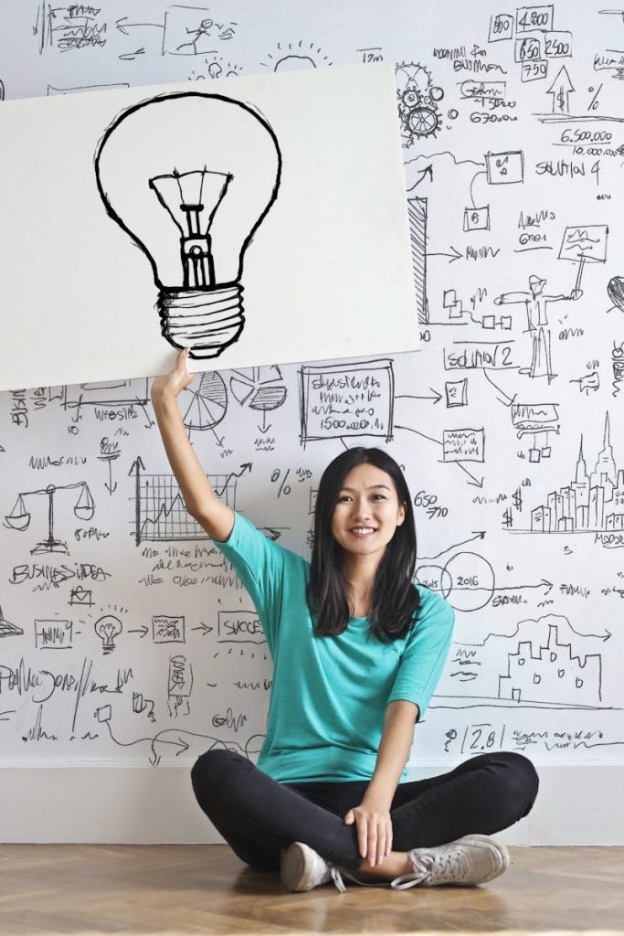 Young woman holds a light bulb drawing against a creative brainstorming wall.