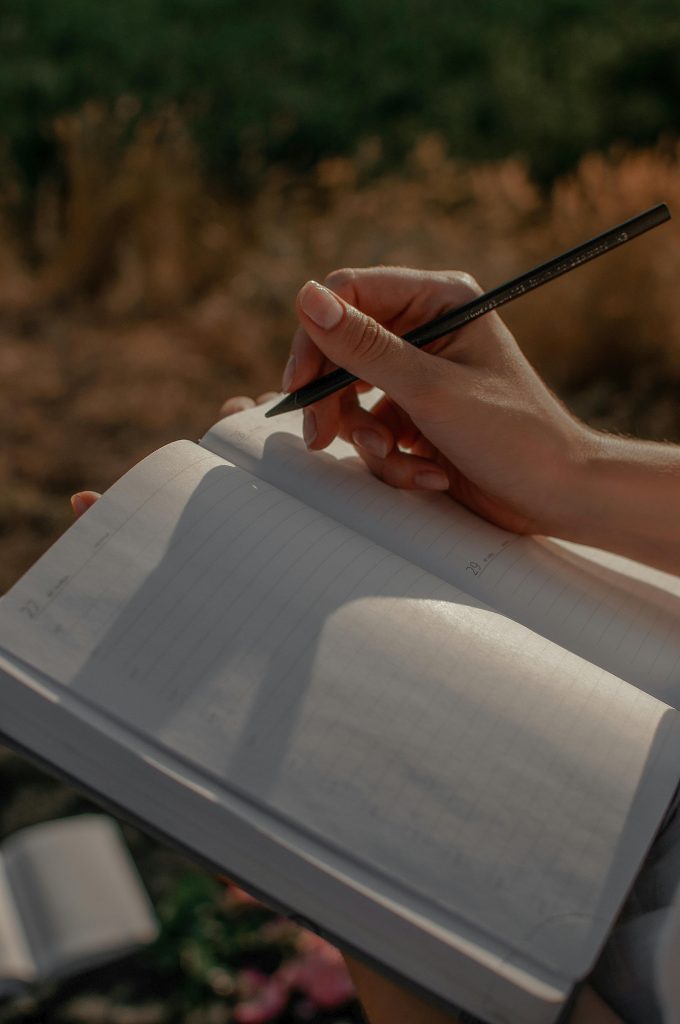 Close-up of a woman writing in a journal outdoors on a sunny day.